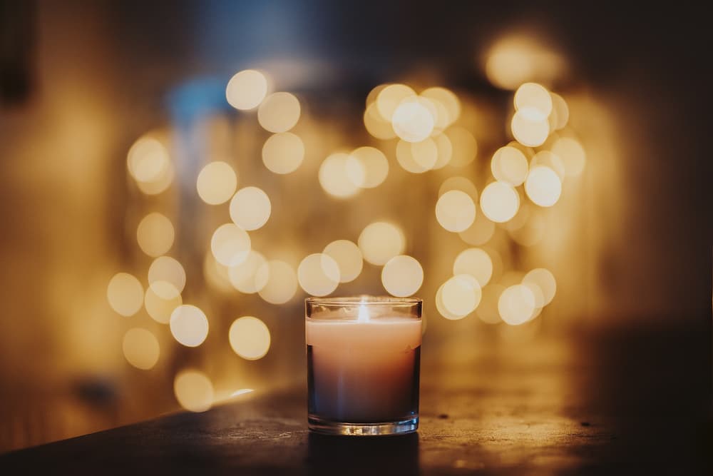 A small lit candle on a table infront of blurred out lights.