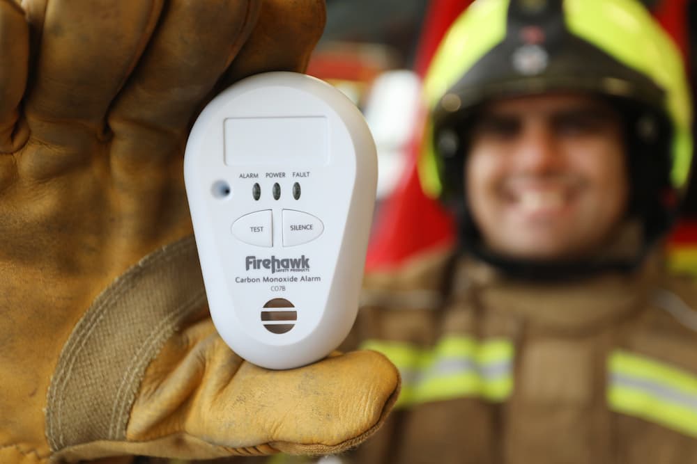 A firefighter holding a carbon monoxide monitor up to the camera