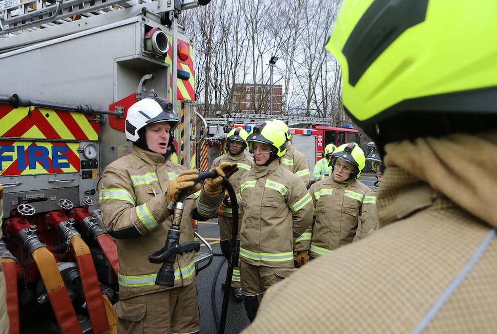 Trainee Firefighters stood around an instructor being shown some equipment