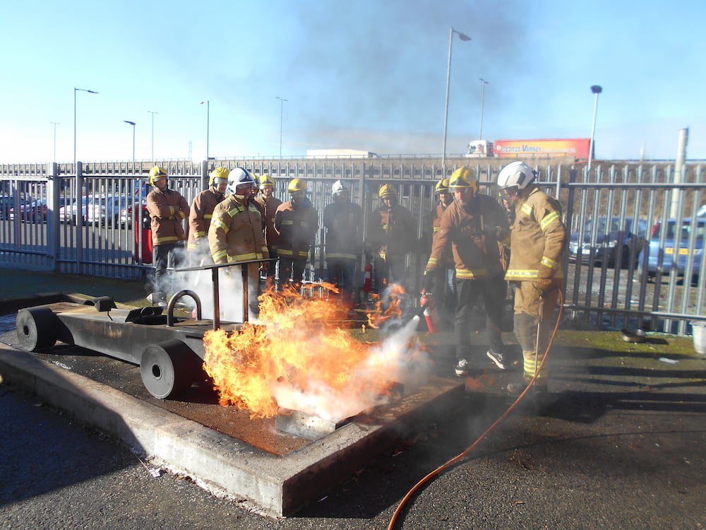 Delegates being shown how to use a fire extinguisher on a fire