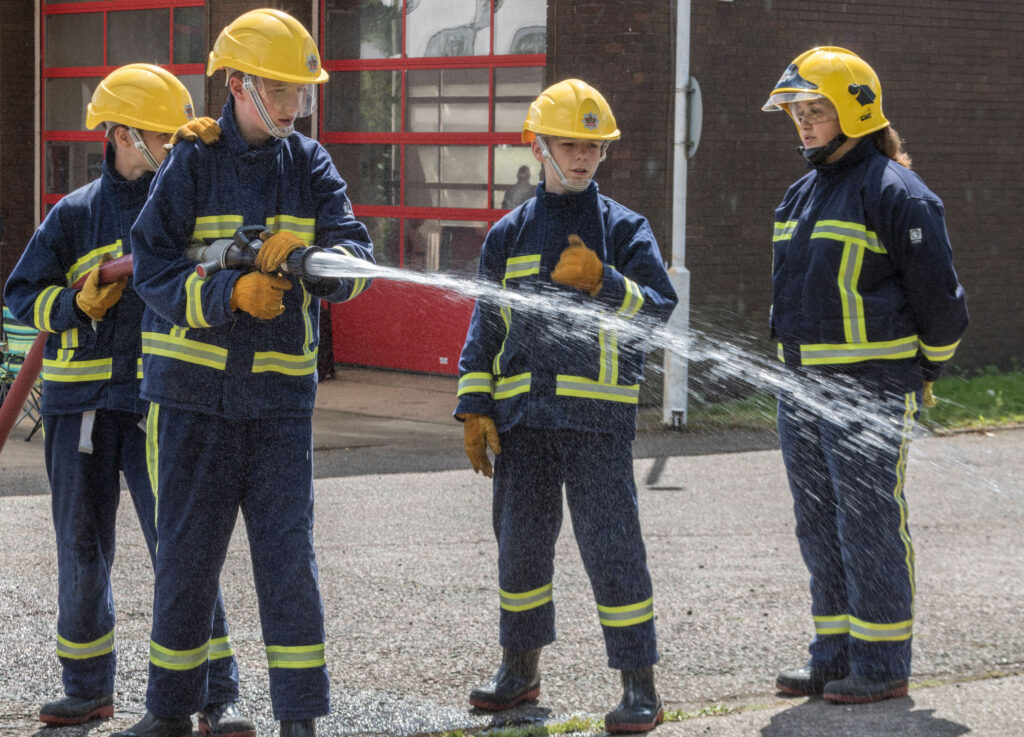 4 Fire cadets in uniform using a water hose
