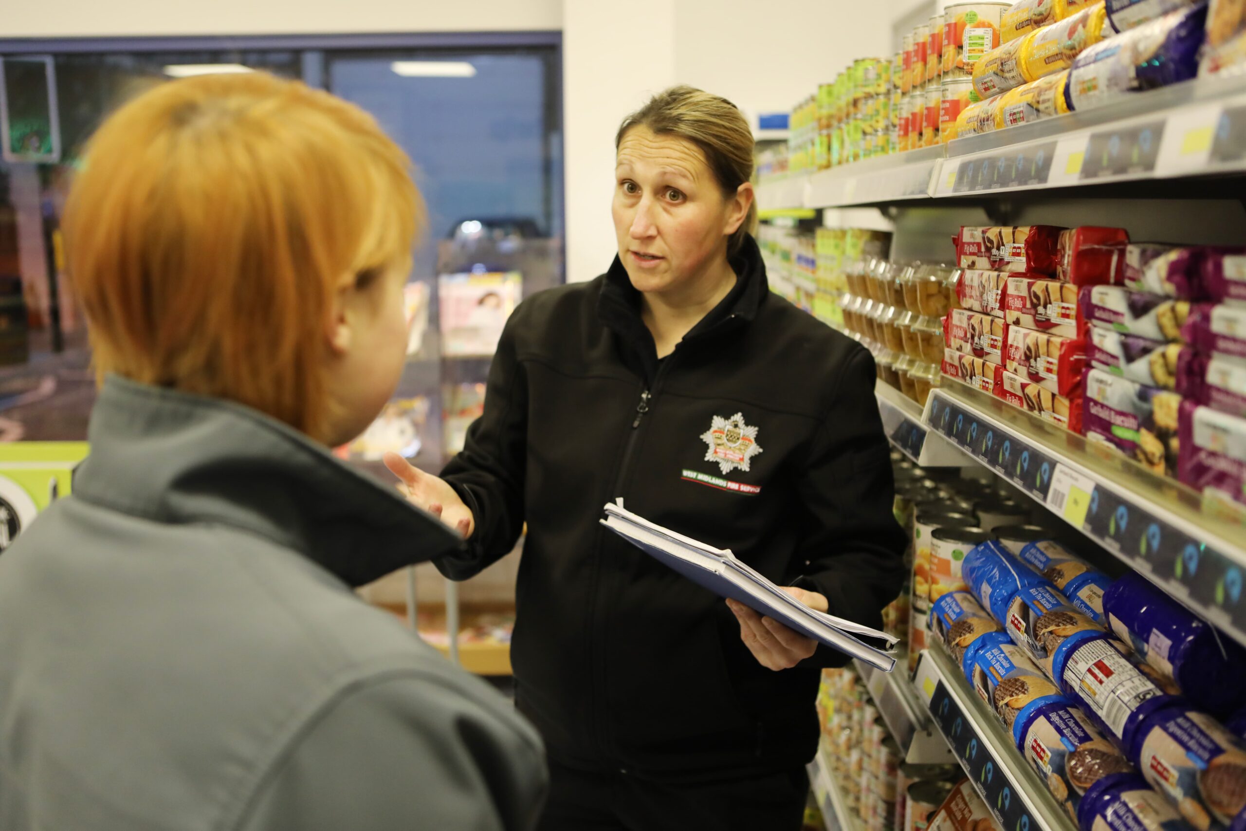 A fire safety officer stood in a retail shop giving the owner advice