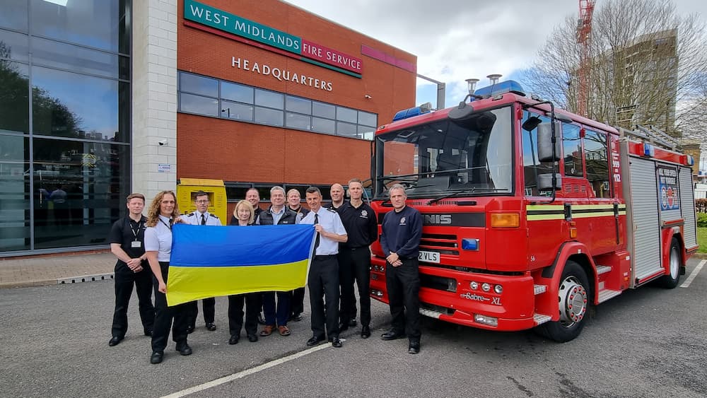 Staff holding up a Ukraine flag in front of the fire engine we're donating