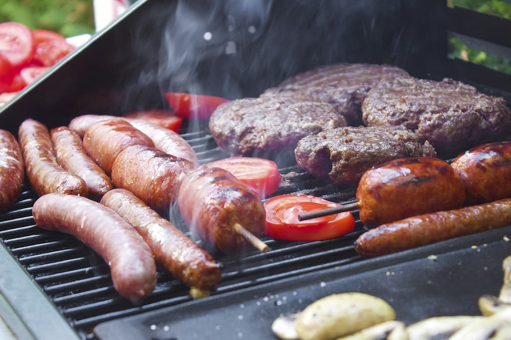 A range of foods like sausages, steaks and tomatoes cooking on a BBQ