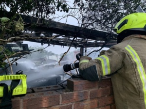 A firefighter leaning over a wall spraying the scrap yard