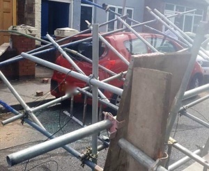 Scaffolding rests on top of a car parked at the kerbside