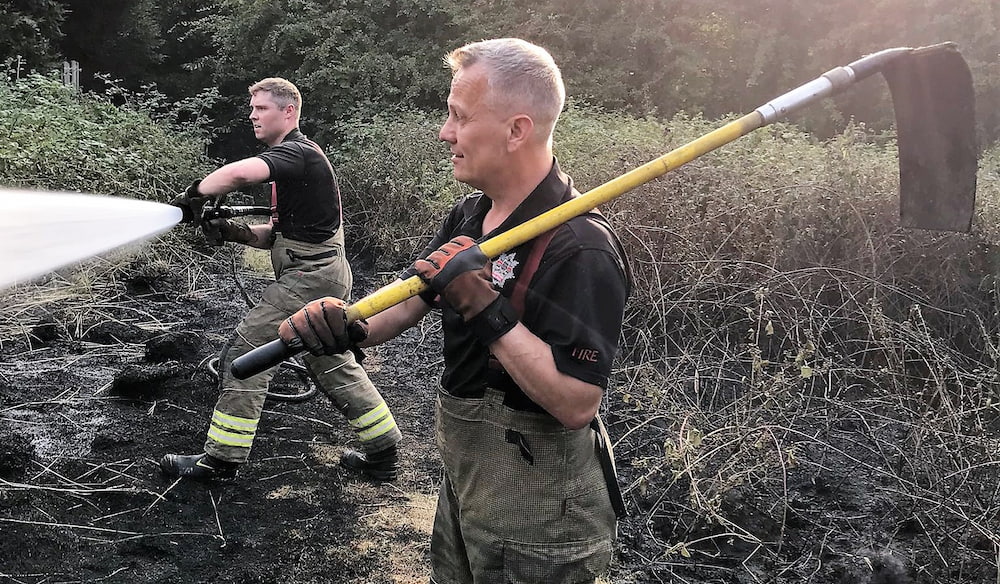 A firefighter uses a hose on scorched ground
