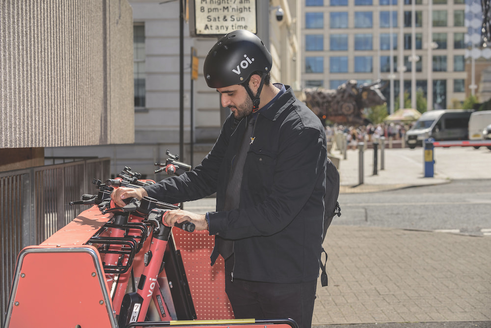 A man wearing a helmet parking a voi scooter in a parking bay