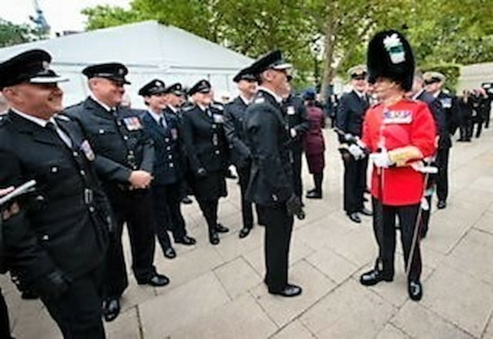 An officer in red tunic and bearskin talks to uniformed personnel involved in the State Funeral procession
