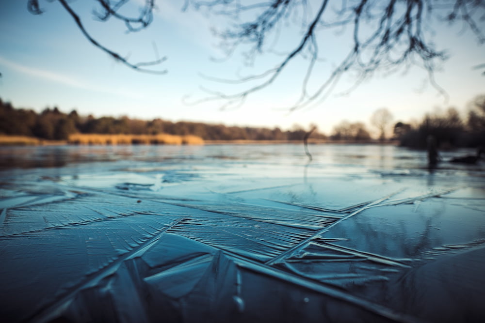 Close up of frozen water on the surface of a lake with an embankment in the distance
