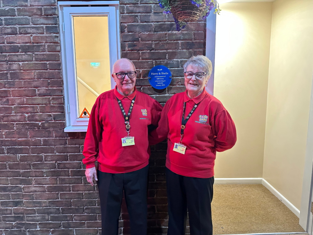 Harry and Sheila stood beside the plaque recognising their achievement of 1000 tours volunteering at Safeside.