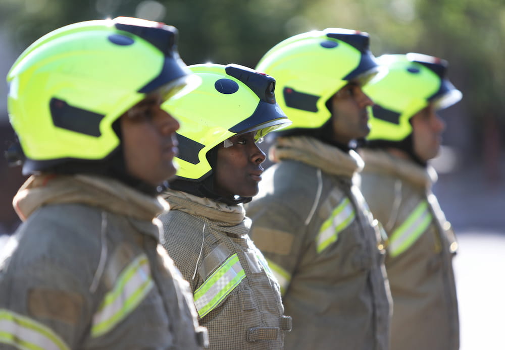 A line of trainee firefighters stand to attention in uniform
