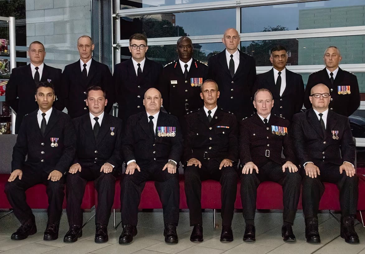 Two rows of firefighters, standing and seated, in smart uniforms, some wearing medals