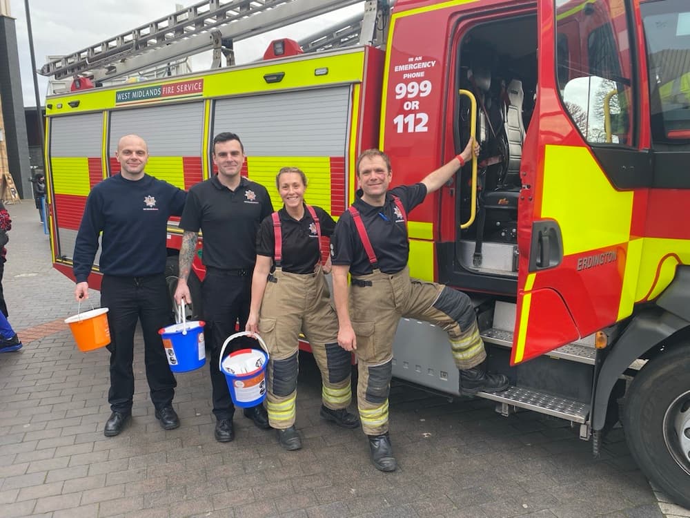 Firefighters pose infront of a fire engine with collection buckets