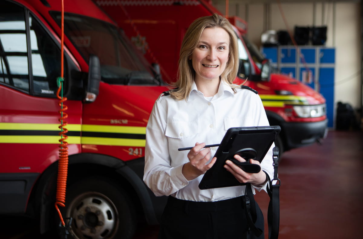 A fire inspecting officer smiling using a tablet in a fire engine bay.