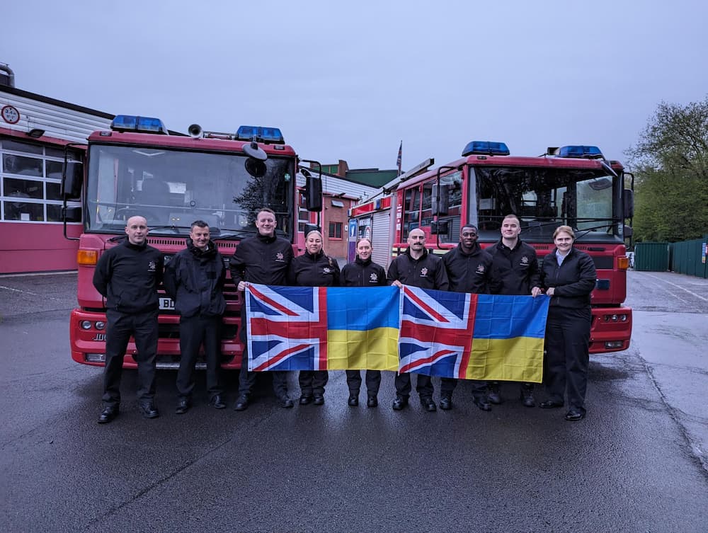WMFS staff members standing infront of two fire engines, holding Ukraine and Britain flags